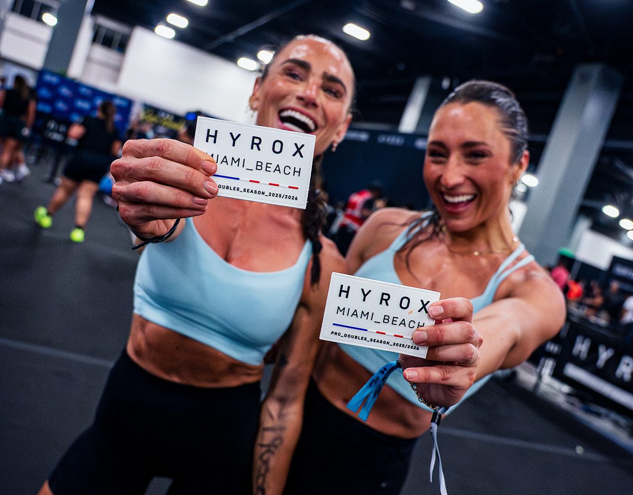 Two athletes holding up HYROX Miami Beach cards on the event floor