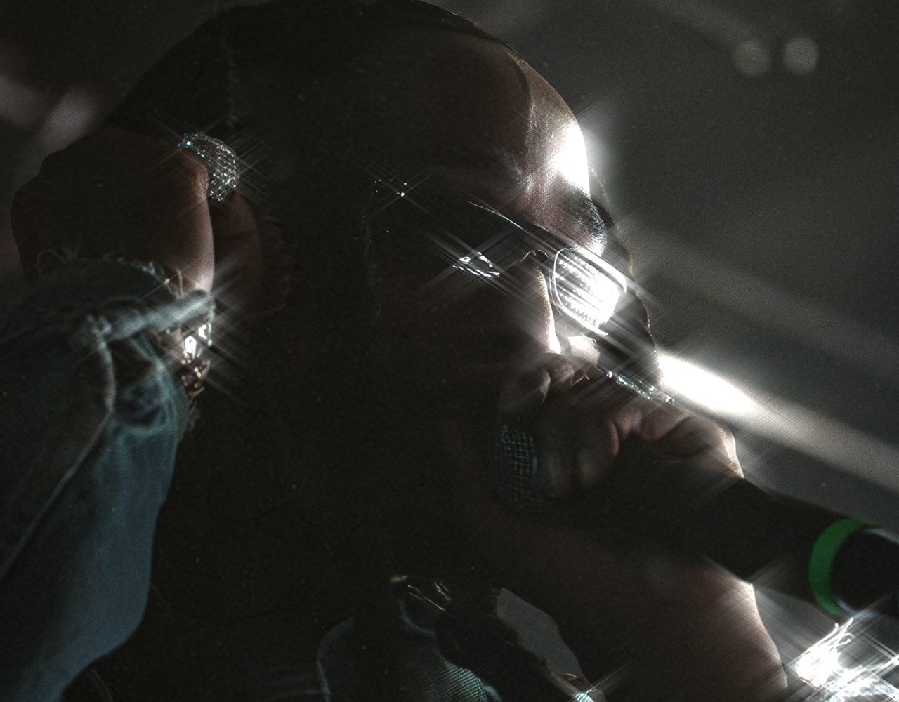 Quavo in silhouette at the microphone, cut by hard stage light