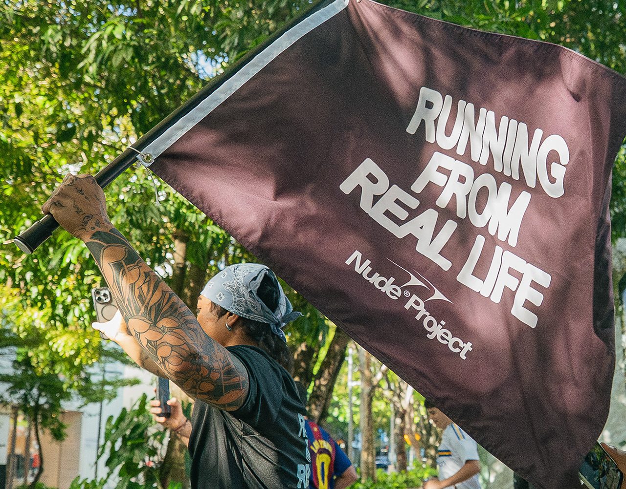 Runner waving a Nude Project flag that reads Running From Real Life, RAWDAWG x NUDE PROJECT