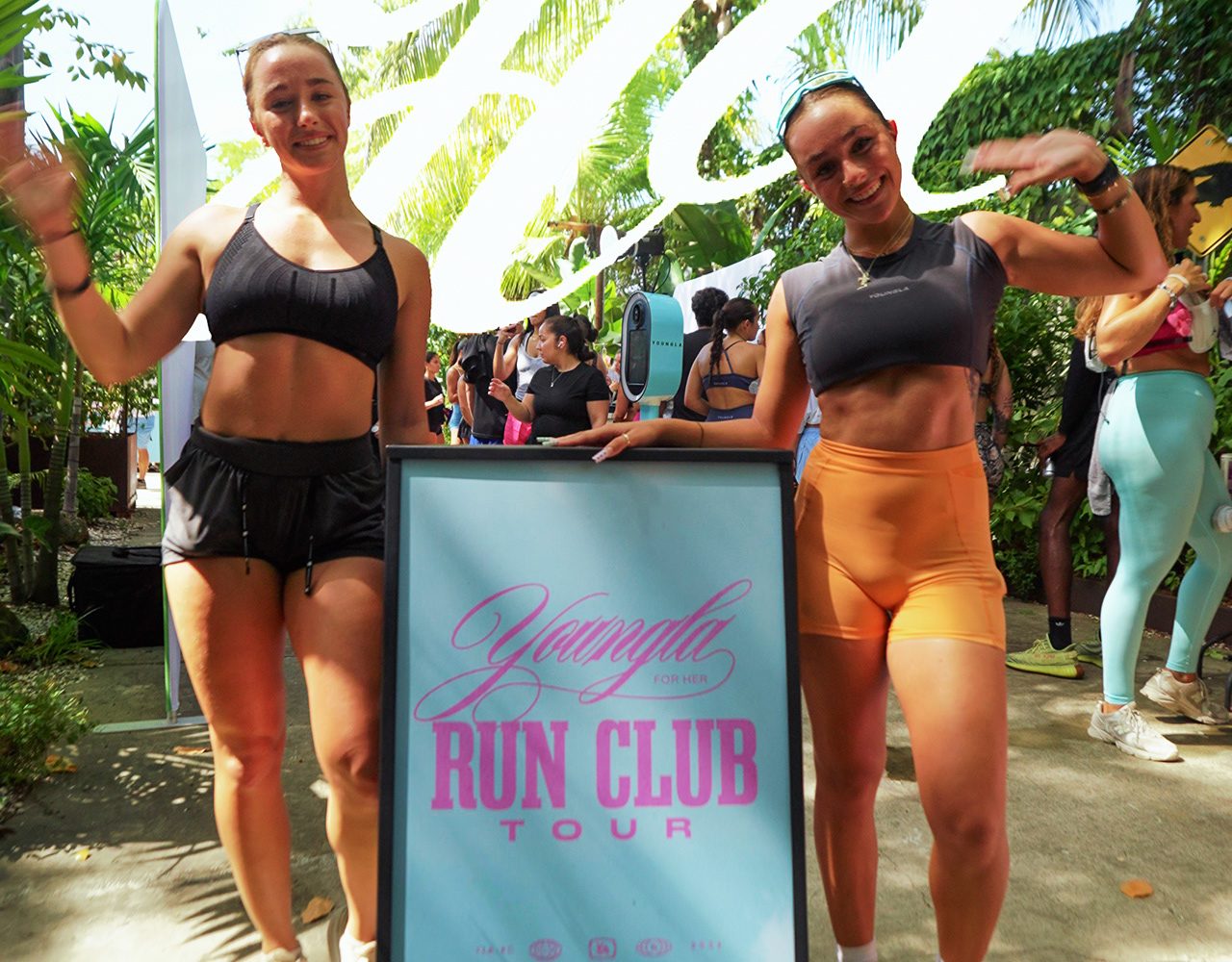 Two athletes posing beside a YoungLA Run Club Tour sign